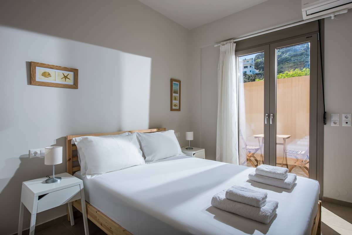 Ein Schlafzimmer mit Bett, Nachttischen, einem Fenster mit Vorhängen und Blick ins Freie.
