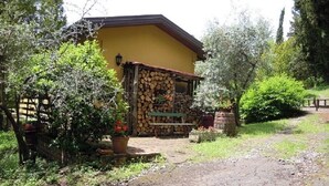 Um edifício rústico com fachada amarela, uma parede de pedra com toras empilhadas e um banco de madeira.