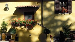 Um edifício amarelo com uma pequena janela, varanda com flores vermelhas e plantas em vasos.