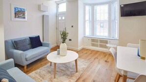 Una sala moderna con un sofá azul claro, una mesa de centro blanca y un comedor con una mesa y sillas blancas.