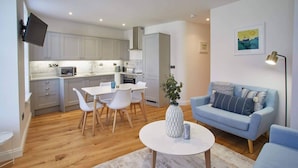Una sala de estar moderna con un sofá azul claro, una mesa de centro blanca y un comedor con sillas blancas y una mesita.
