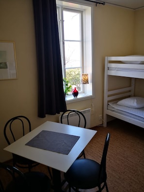 Una habitación con literas, una mesa con sillas, una ventana con cortinas y un radiador.