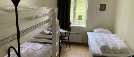 A room with bunk beds, a desk, a chair, a window with a view of a red barn, and a radiator.