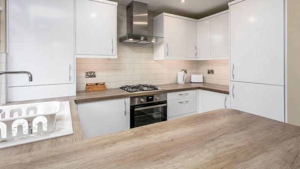 Una cocina moderna con armarios blancos, una campana extractora de acero inoxidable, un horno empotrado y una encimera de madera.