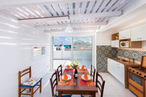 Un comedor con una mesa dispuesta para cuatro, una cocina con salpicadero decorado y vistas a través de la puerta de vidrio.