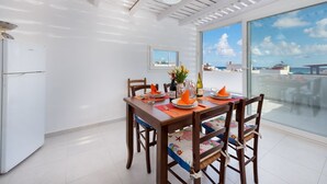 Un comedor con una mesa dispuesta para cuatro, un refrigerador y un amplio ventanal con vista al mar.