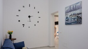 Una sala de estar con un gran reloj de pared, un sofá, un sombrero y un cuadro.