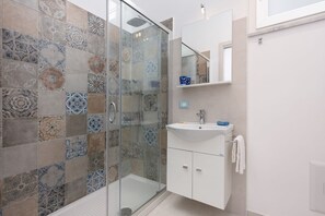 Un baño con cabina de ducha de vidrio, un lavabo blanco y un espejo encima.
