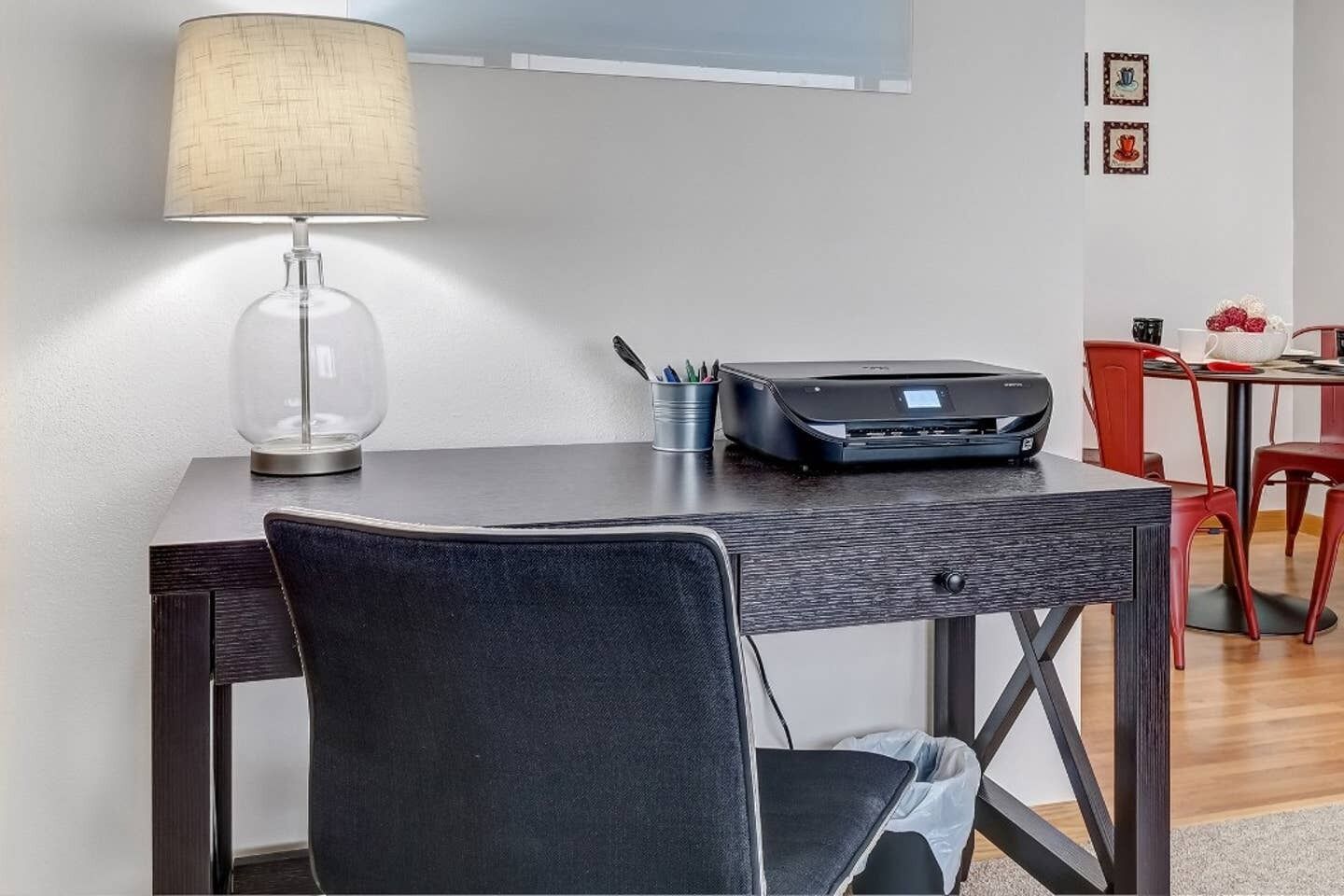A modern office space with a desk, chair, lamp, printer, and red chairs.