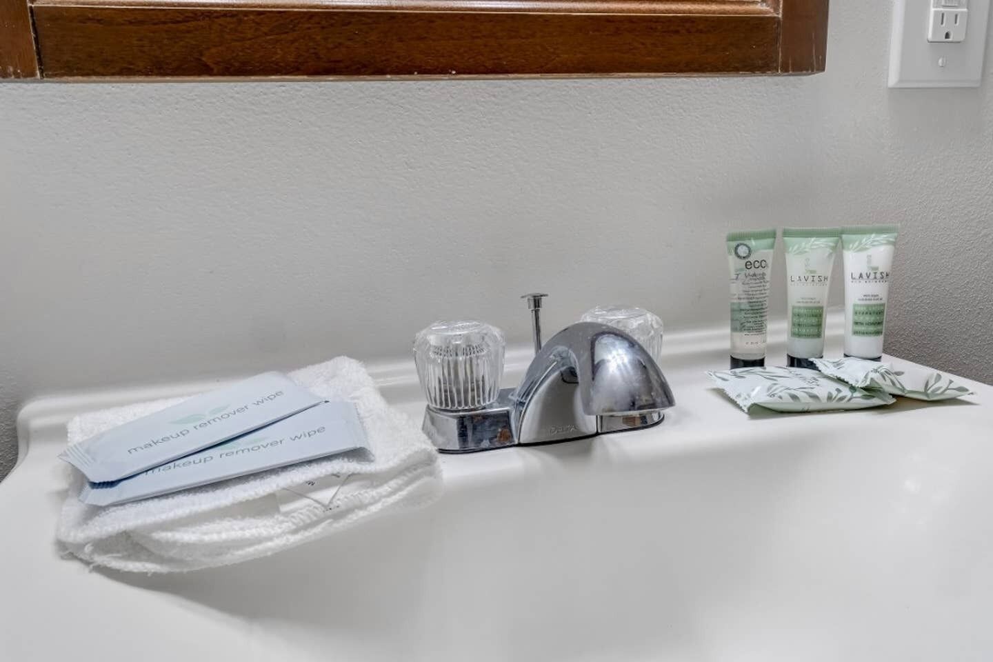 Ein Badezimmerwaschbecken mit einem handlichen Abschminktuch, einem Delta-Wasserhahn und zwei Tuben Lavish Körperwäsche.