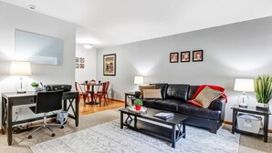 A modern living room with a black leather sofa, a dining table with red chairs, a desk with a chair, and a coffee table.