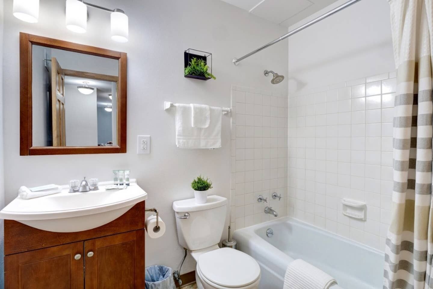 A bathroom with a white sink, mirror, toilet, and bathtub.