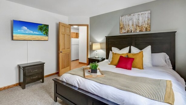 A bedroom with a bed, bedside table, lamp, and a painting of a beach scene.