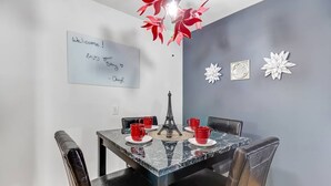 Un coin repas avec une table en marbre, quatre chaises en cuir noir et une petite maquette de la Tour Eiffel. Sur la table, on peut voir deux tasses rouges, et sur le mur, une inscription « Bienvenue ! » ainsi que des fleurs décoratives.