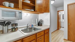 Une cuisine avec des meubles de rangement en bois, un four à micro-ondes, un évier et un porte-épices.