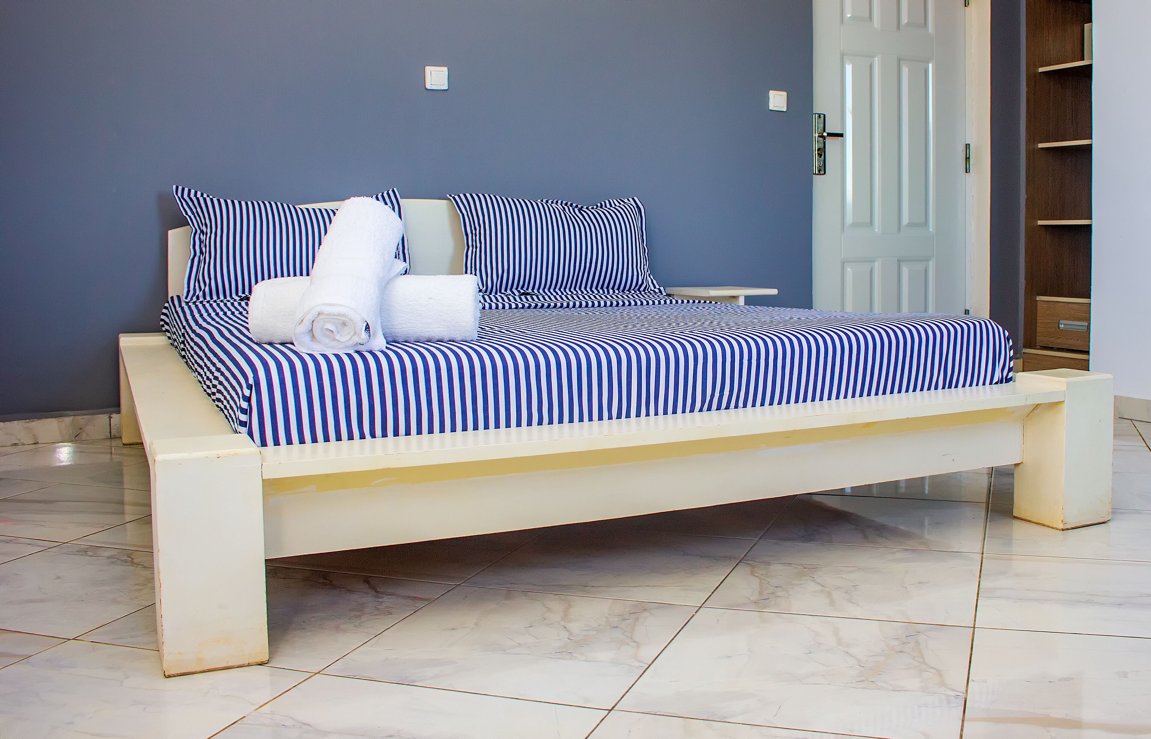 Una cama con ropa de cama a rayas, una mesita de noche y un armario de madera en una habitación con suelo de baldosas.