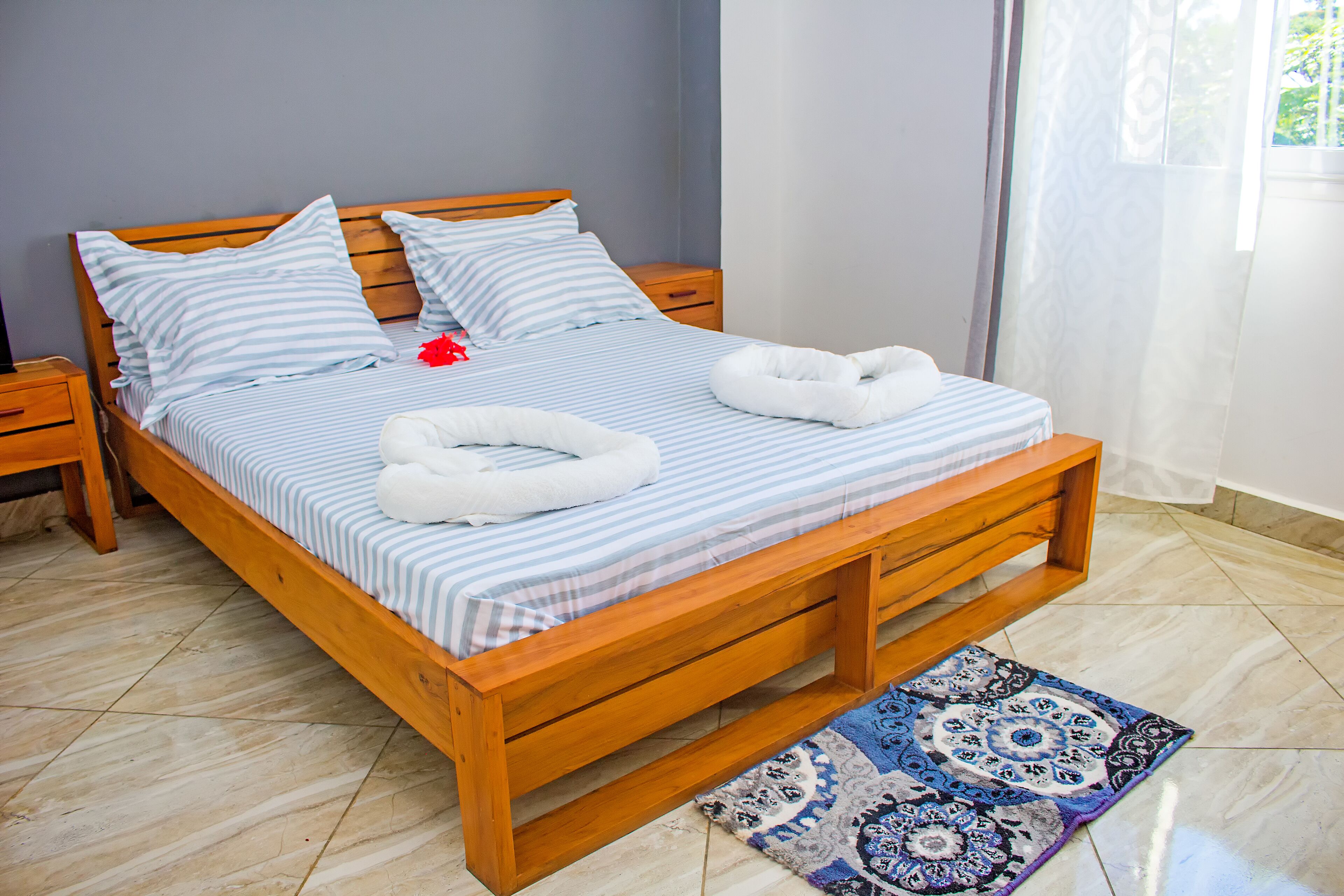 A wooden bed with striped bedding, two pillows, and two white towels.