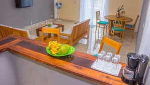 Una cocina con mostrador de madera, un bol de plátanos, una cafetera y una zona de comedor con sillas y una mesa.