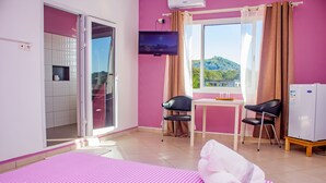 Habitación de hotel con cama, televisión, mesa y sillas, y vista a una montaña.