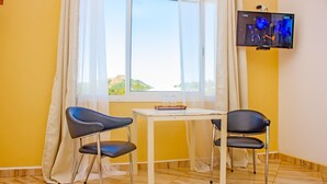 Una habitación con ventana, dos sillas, una mesita y un televisor en la pared.