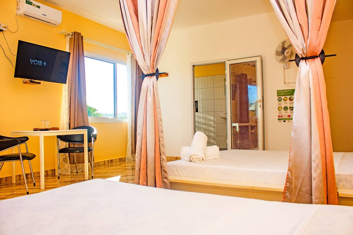 A hotel room with a bed, a desk with chairs, a television, and curtains.