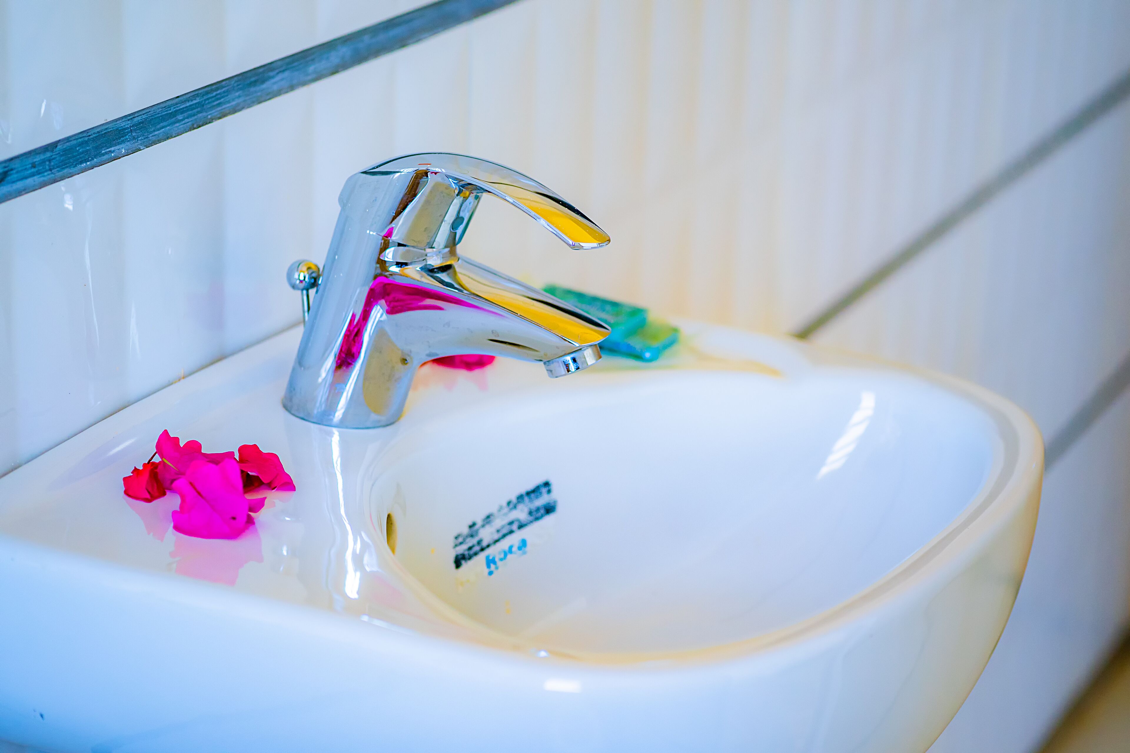 A bathroom sink with a chrome faucet, a soap dish, and a few rose petals.