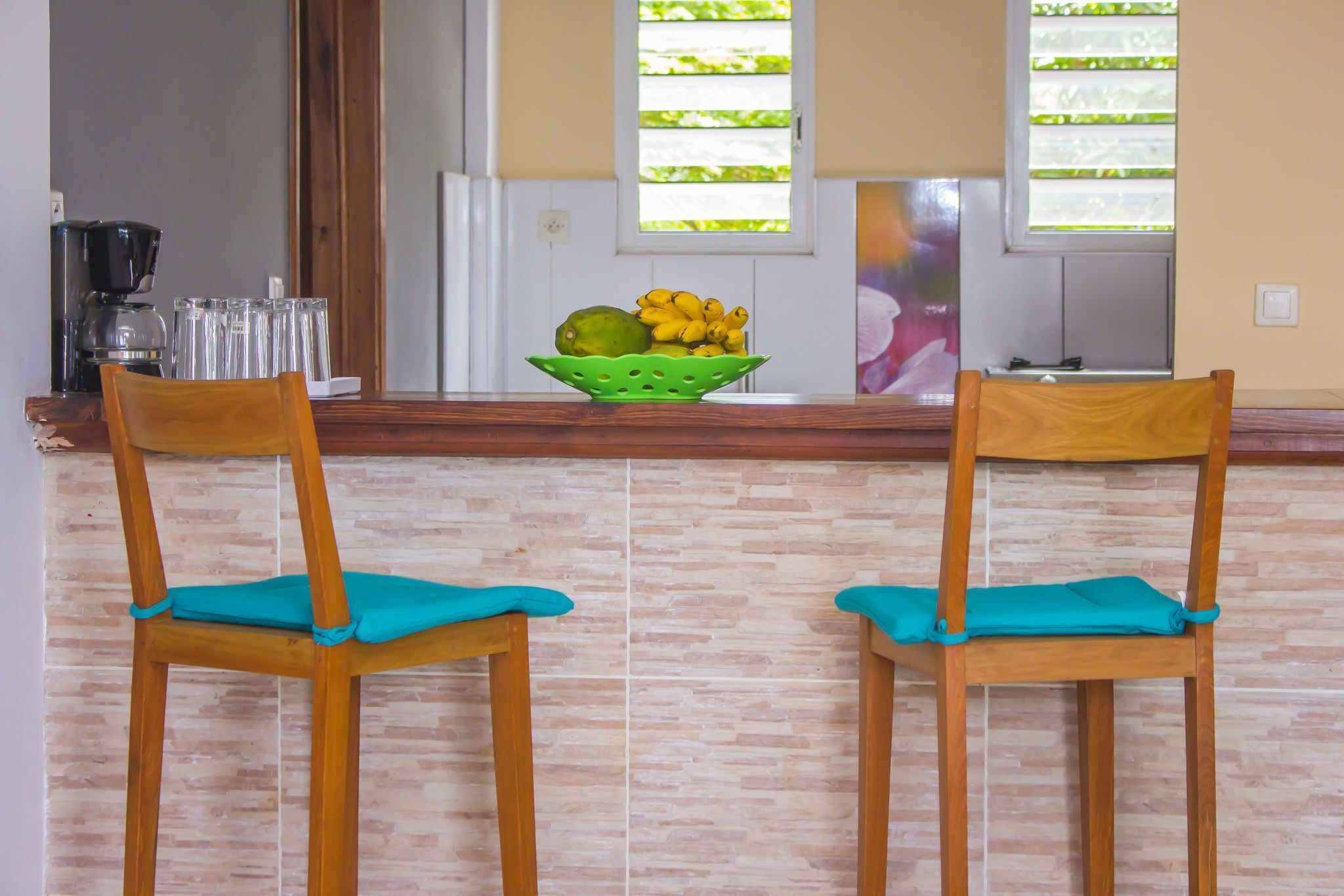 A kitchen with two wooden chairs, a green fruit bowl, and a coffee maker.