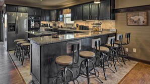 Una cocina moderna con armarios oscuros, electrodomésticos de acero inoxidable, una isla de granito con taburetes altos e iluminación colgante.