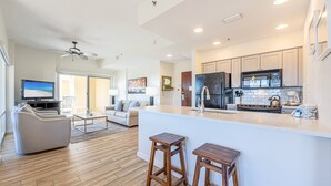 A modern kitchen with a central island, wooden stools, and a dining area with a sofa and coffee table. - Private Balcony ~ Lockout Unit ~ Fully Equipped Kitchen ~ Kitchenette (Miramar Beach)