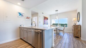 A modern kitchen with a central island, stainless steel appliances, and a view to a dining area. - Private Balcony ~ Lockout Unit ~ Fully Equipped Kitchen ~ Kitchenette (Miramar Beach)