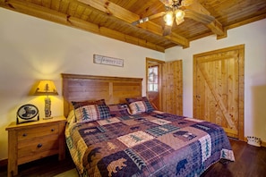 Une chambre avec un plafond en bois, un lit recouvert d’une courtepointe, une table de chevet avec une lampe et une porte en bois.