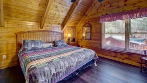 Ein Schlafzimmer einer Holzhütte mit einem großen Bett, einem Fenster mit Jalousien und einem Deckenventilator.