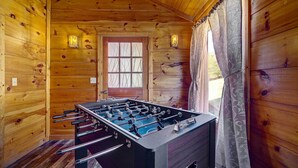 Ein Zimmer mit Holzboden, einem Kicker, einem Fenster mit dekorativem Vorhang und einer Tür mit Fenster.