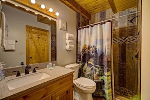 A bathroom with a wooden door, a sink with a mirror, a toilet, and a shower with a decorative curtain. - Tennessee Charm (Sevierville)