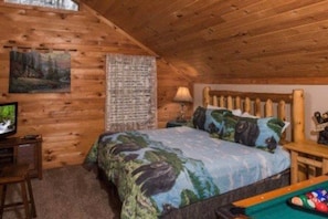 Ein Holzhüttenraum mit einem Bett, einem Fernseher und einem Billardtisch.