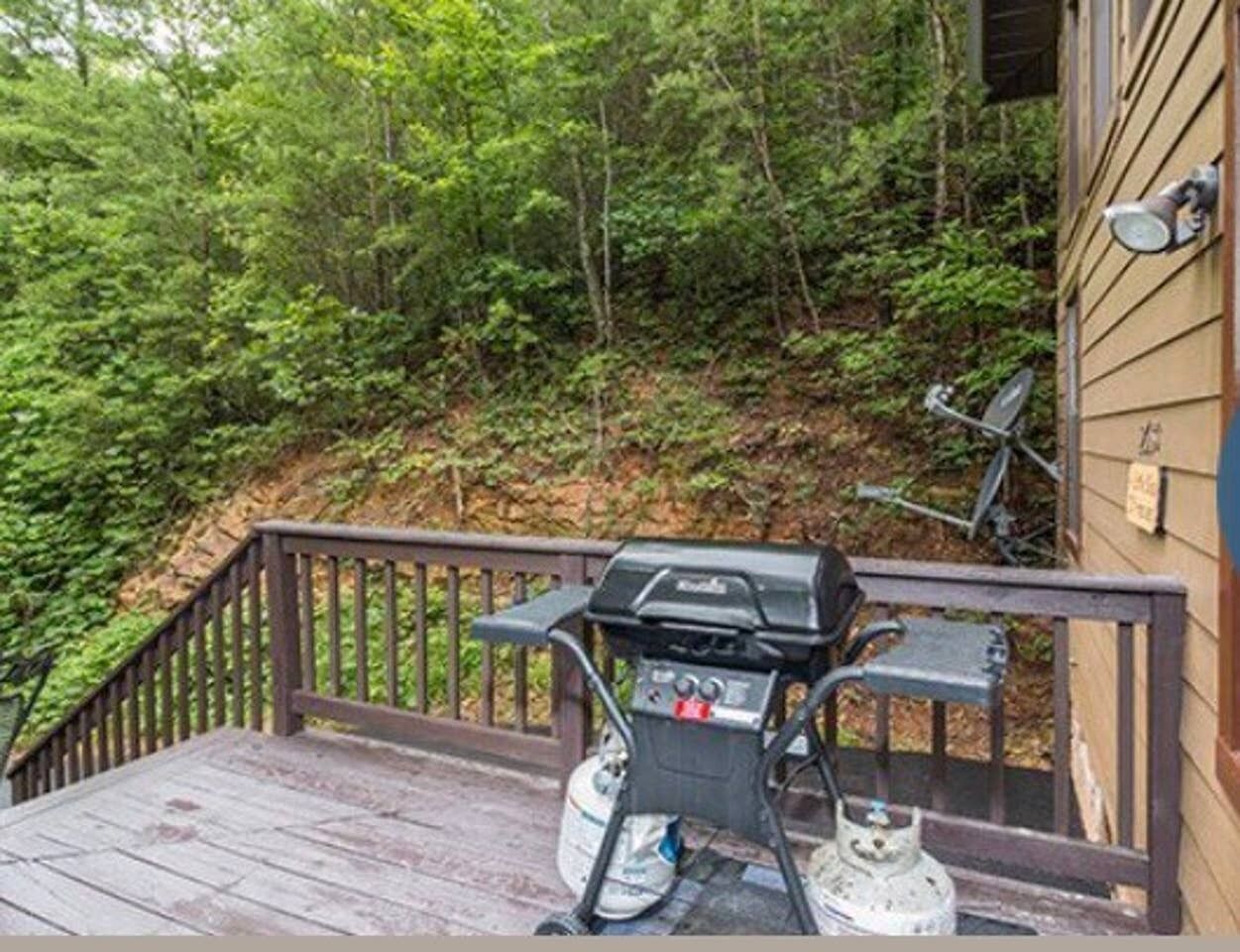 A wooden deck with a barbecue grill and propane tank.