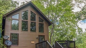 A two-story wooden cabin with a stone foundation, a front porch, and a staircase leading to a deck. - The Heart of Tennessee (Sevierville)