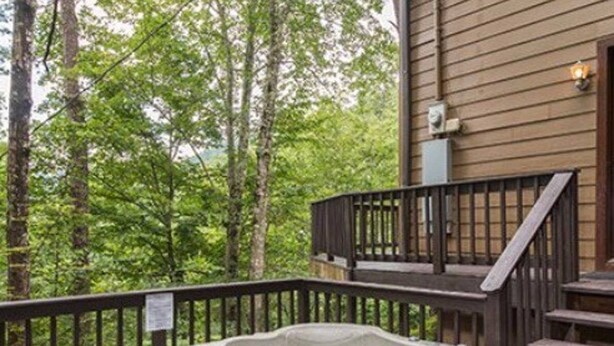 A hot tub on a wooden deck with a railing, surrounded by trees. - The Heart of Tennessee (Sevierville)