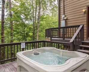 Ein Whirlpool auf einer Holzterrasse mit Geländer, umgeben von Bäumen.