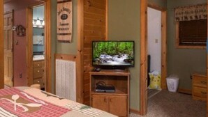 A room with a wooden ceiling, a television on a wooden stand, a bed with a red and white patterned bedspread, and a wooden door with a sign above it. - The Heart of Tennessee (Sevierville)