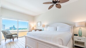 Een slaapkamer met een groot bed, een stoel, een nachtkastje en een plafondventilator.