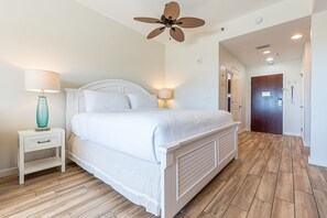 A bedroom with a bed, nightstands, a ceiling fan, and a wooden floor. - Studio ~ Kitchenette ~ Gulf Views ~ Community Pool (Miramar Beach)