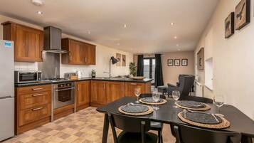 A modern kitchen with wooden cabinets, stainless steel appliances, and a dining area with black chairs and woven placemats.