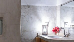 Un baño con pared de mármol, armarios de madera, un lavabo con espejo y zona de ducha.
