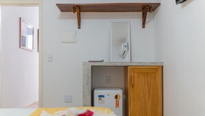 Una habitación de hotel con una cama, un armario de madera, un refrigerador blanco y un estante de madera sobre la cama.