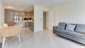 Un apartamento moderno con comedor, un sofá gris y una cocina al fondo.