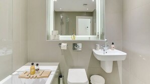 Un baño moderno con un espejo grande, un lavabo, un inodoro y un mueble de tocador con artículos de aseo.