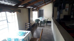 A room with a table covered by a white tablecloth with blue text, a wooden chair, and a window with bars. - Queens Village Hotel (Nakuru)