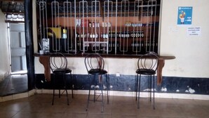 A bar area with metal bars, three chairs, and a shelf with bottles. - Queens Village Hotel (Nakuru)
