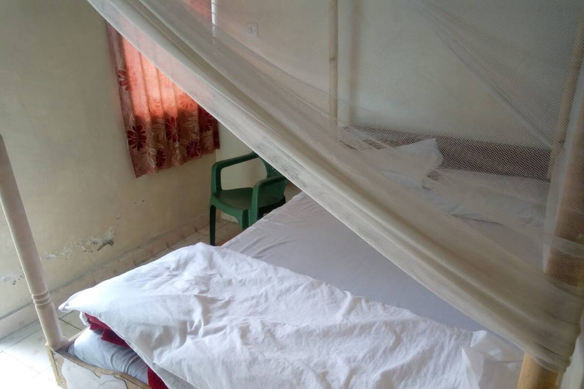 A single bed with a mosquito net, a green chair, and a window with a curtain.
